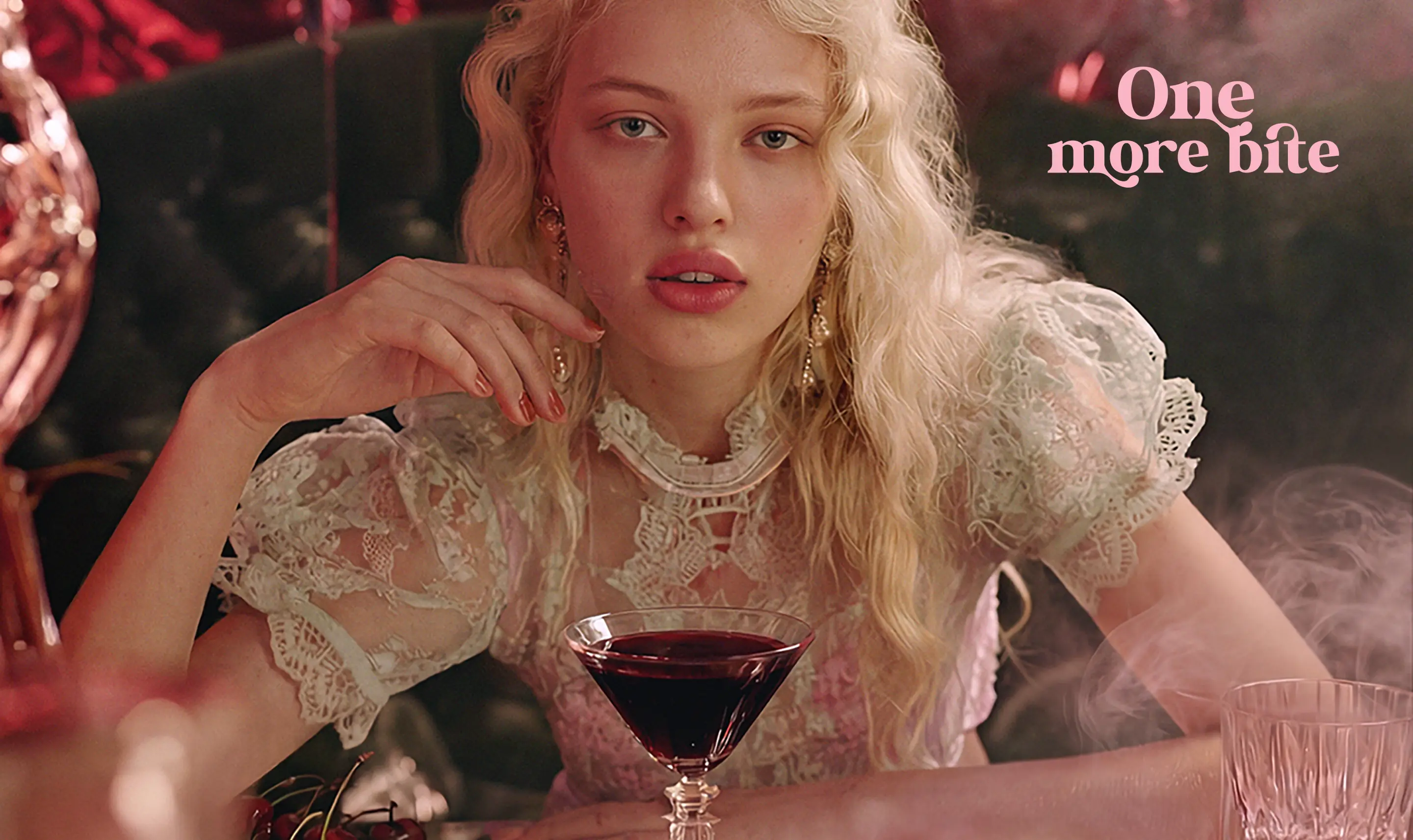 Modelka przy stole z czereśniami i kieliszkiem wina, z mgiełką perfumowaną ONLYBIO One More Bite leżącą na stole wśród owoców.