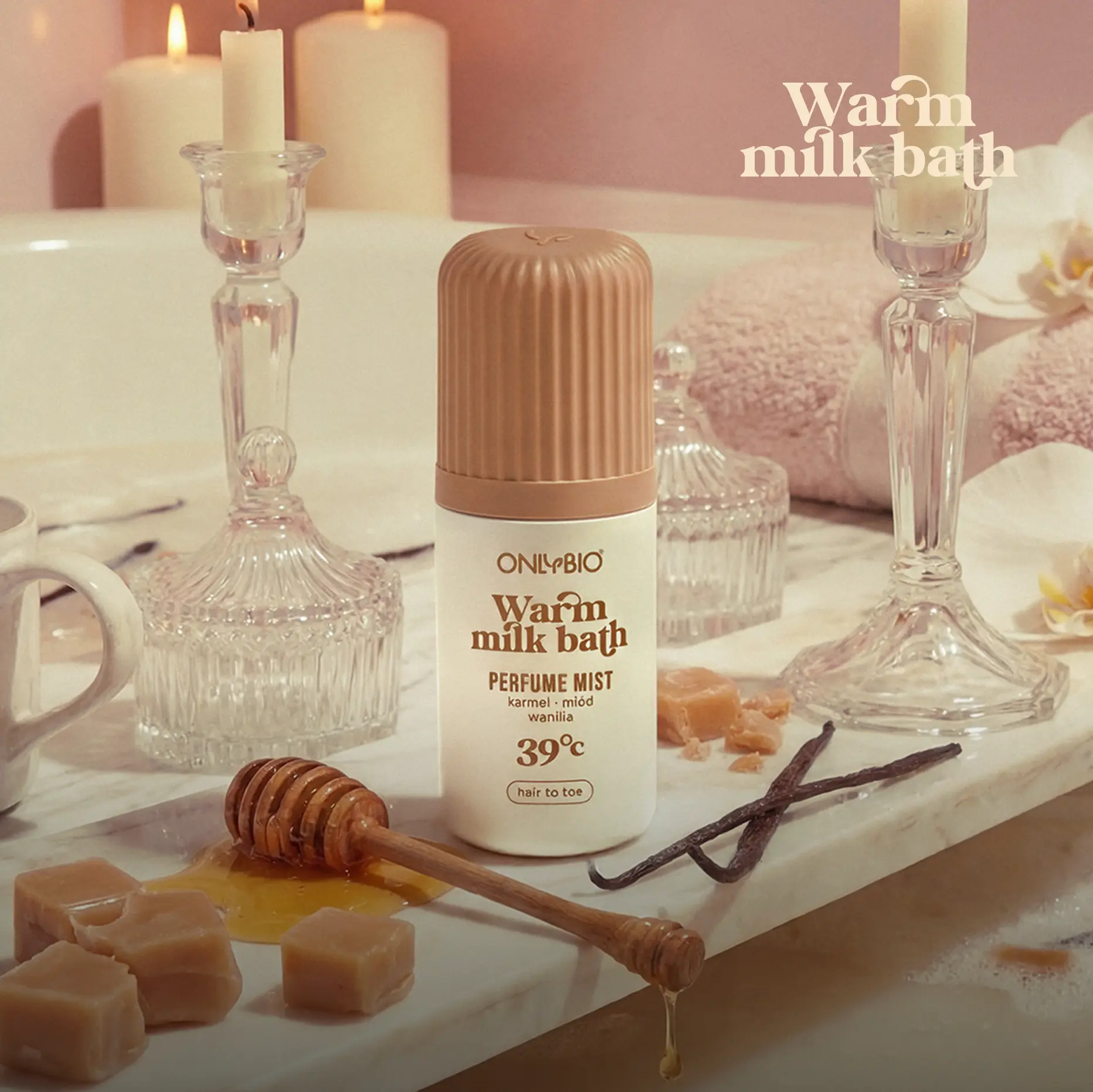 Mgiełka perfumowana ONLYBIO Warm Milk Bath na brzegu wanny, obok miodu, wanilii i kostek karmelu.
