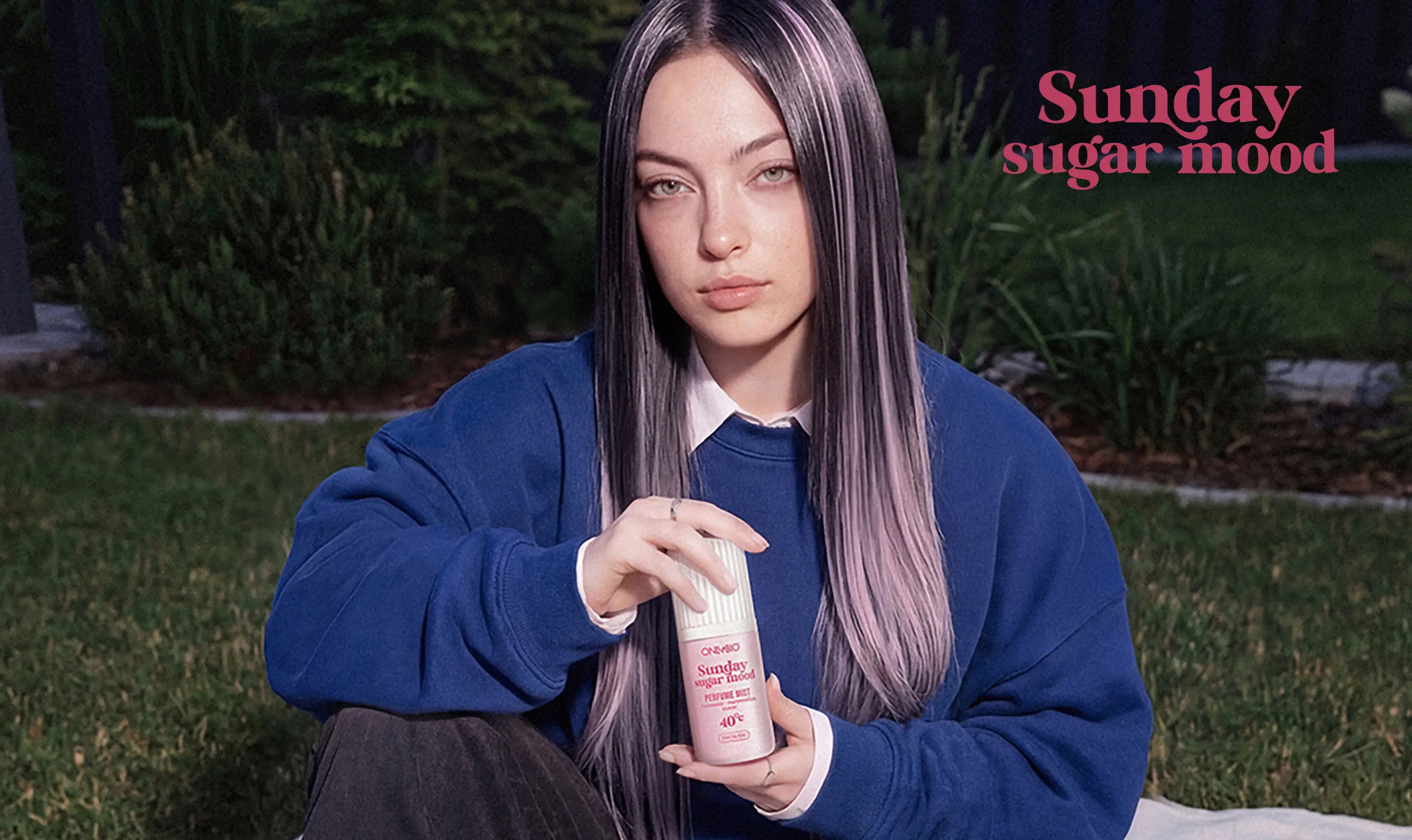 Modelka w bluzie siedzi na pikniku w ogrodzie, otoczona truskawkowymi deserami, trzymając mgiełkę perfumowaną ONLYBIO Sunday Sugar Mood.