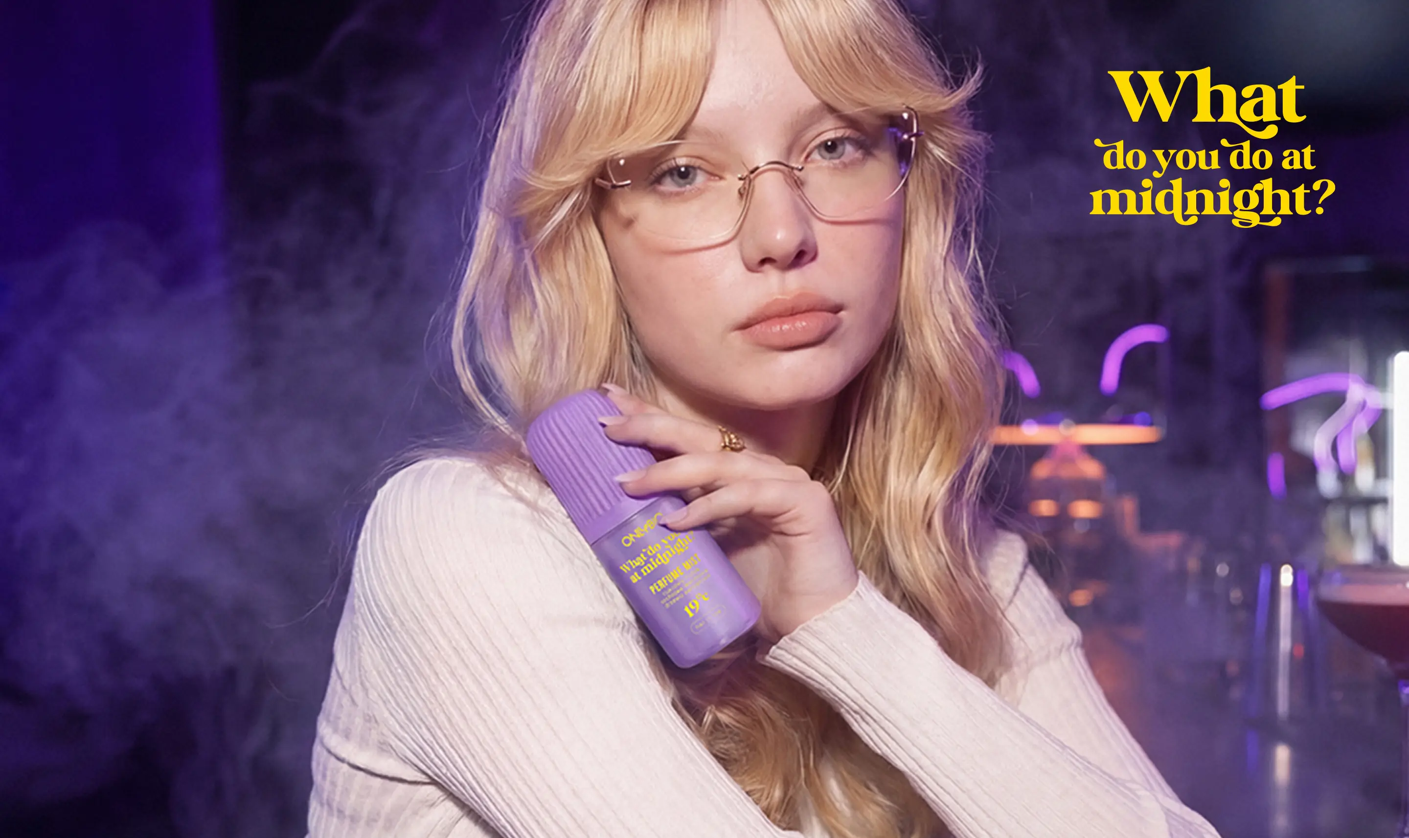 Modelka w okularach siedzi przy barze w klubowym wnętrzu, trzymając mgiełkę perfumowaną ONLYBIO What Do You Do at Midnight?.