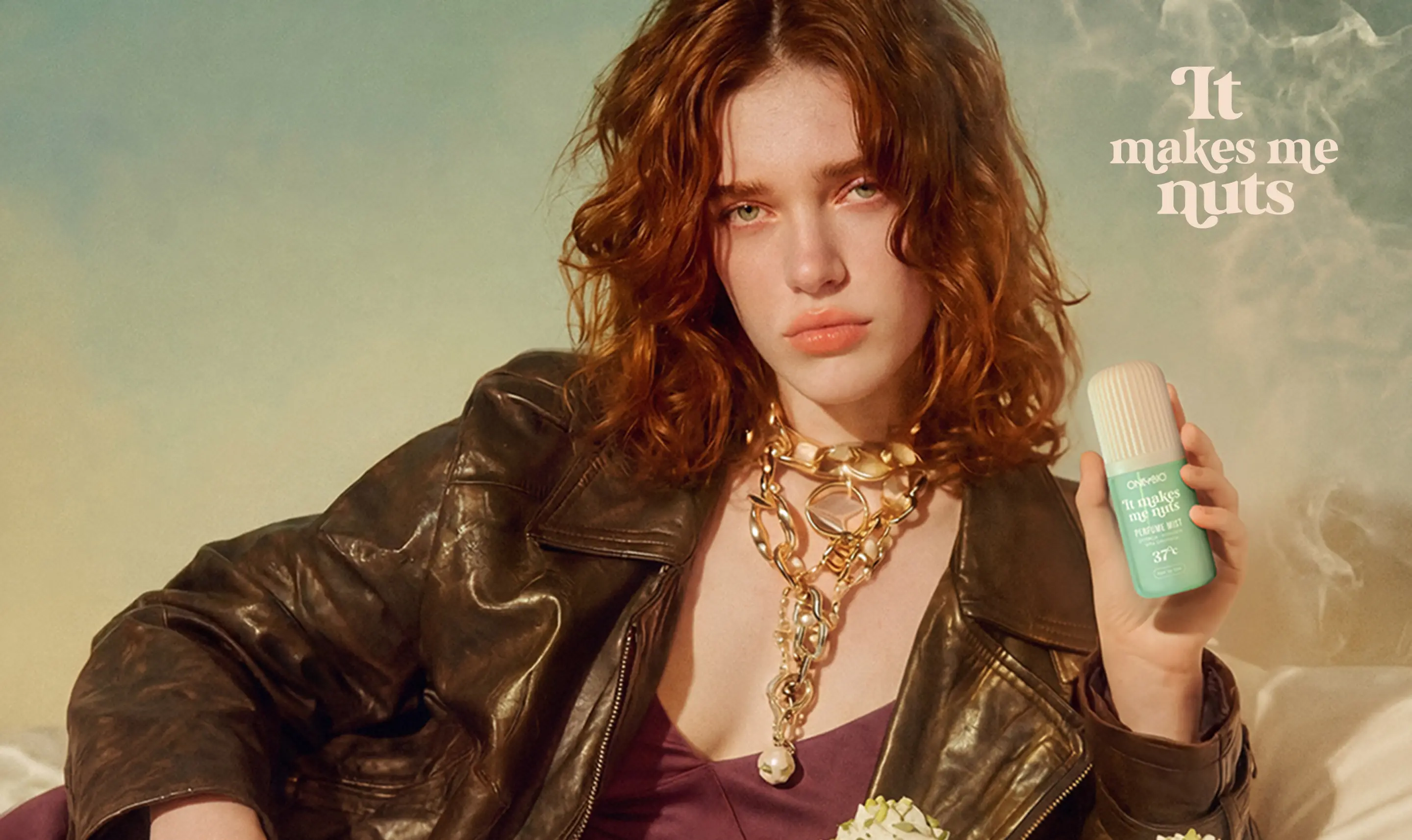 Modelka w skórzanej kurtce trzymająca zieloną mgiełkę perfumowaną ONLYBIO It Makes Me Nuts, siedzi przy stole z pistacjowymi rogalikami i deserami.